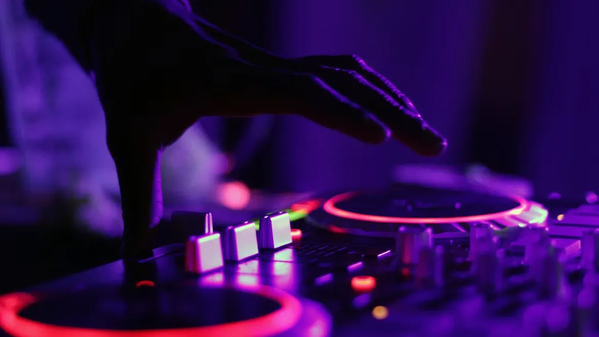 紫のネオンに照らされた DJ 機材のジョグに手を添えている様子